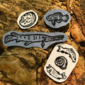 Four iron-on denim and white patches featuring black ink linoleum block prints of a mollusk, a snail shell with a trout and a bass, a gar, and a pygmy sunfish.