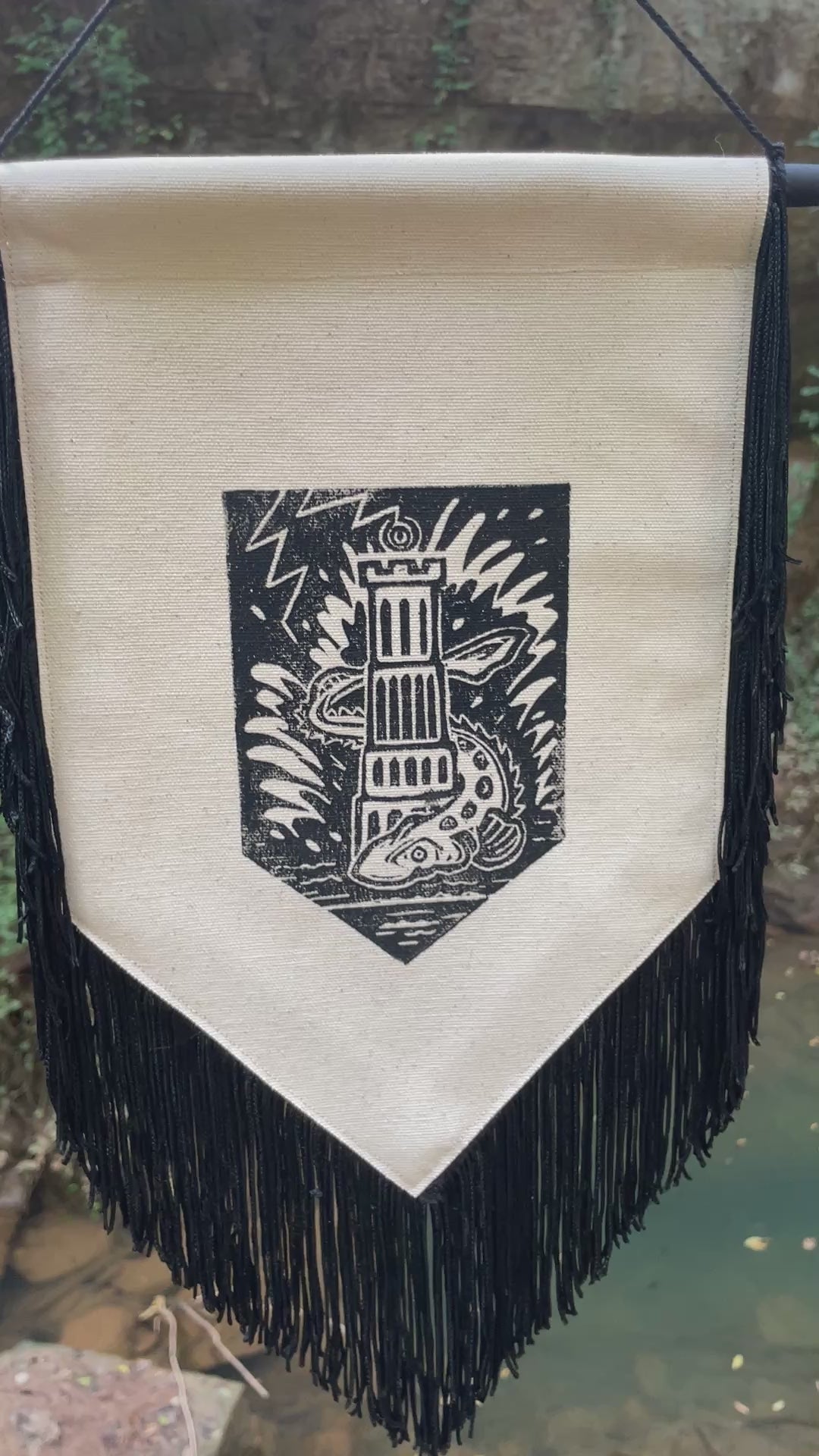 A video of the Tower Banner hanging outside in a forest setting, the fringe on the bottom of the canvas banners blowing in the breeze.